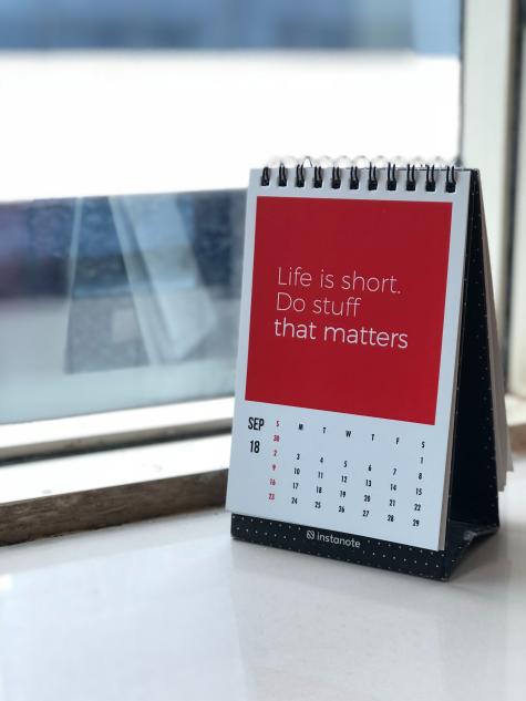 A white and red calendar sits on a window ledge displaying the month of September. Above the dates there is a large red box which says ' Life is short. Do stuff that matters.'