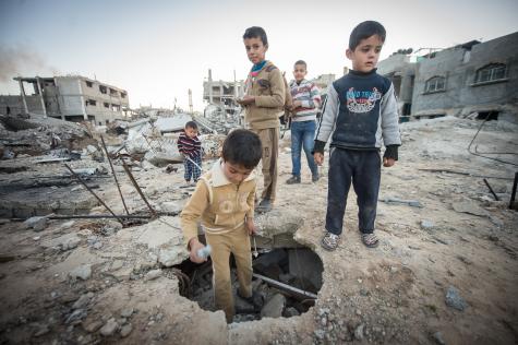 Five young Palestinian children stand in the destruction of Gaza surrounded by rubble and crumbling buildings