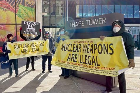 Protesters in the US gather infront of a major bank demanding that they divest from nuclear weapons. They hold large yellow banners stating that nuclear weapons are illegal.