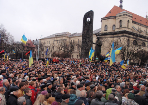 Anti-governmental protesters gather outside of Kyiv. Under a grey sky thousands of protesters hold blue and yellowUkraine flags.