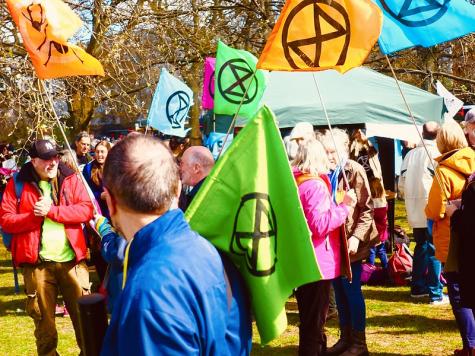 Extinction Rebellion protesters gather in Hyde Park, London. They carry large colourful flags with the sandtimer XR symbol on.