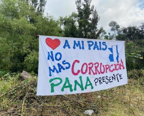 A white sheet has been hung between trees at a roadblock in Guatemala where protesters are fighting for democracy. It has been painted to say 'No more corruption in my country, Pana is present'.