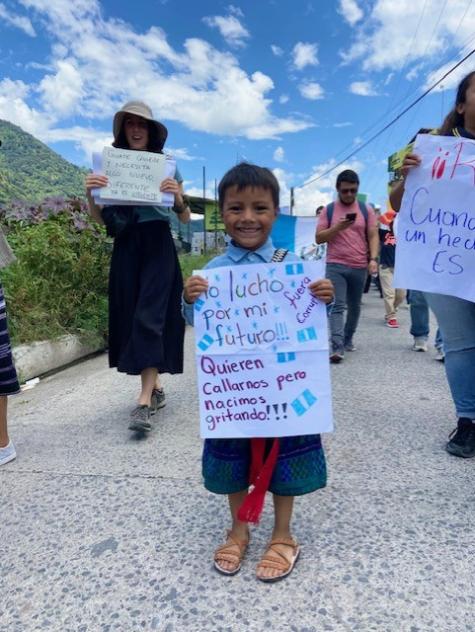 An adorable young Guatemalan boy stands in the street holding a sign which says 'I am fighting for my future'. He is part of a prodemocracy protest 