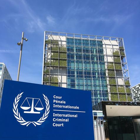 Photo of the International Criminal Court (ICC) taken in 2018 in Den Haag. A multistorey glass building with plants growing from the balconies with the blue ICC logo in the foreground.