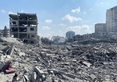 Damage from an Israeli airstrike on the El-Remal area in Gaza City on 9 October 2023. Gry destroyed buildings lie under a blue sky.