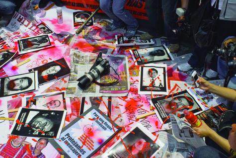A protest by journalists in Mexico where rising violence has resulted in the death of many in the industry. There are photos of missing and murdered journalists on the floor covered in red paint with a camera sitting in the middle.