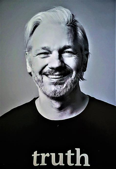 Black and white portrait of journalist Julian Assange. He is smiling at the camera and wearing a black tshirt with the word 'Truth' written in white
