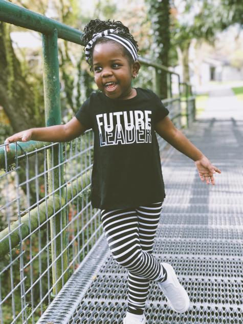 Cute young black girl stands on a bridge wearing a black tshirt that says future leader