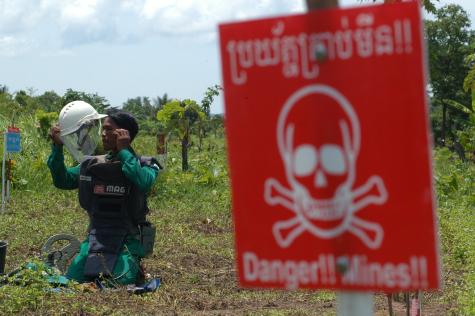 A man in full protective gear temporarily removes his helmet while working to remove landmines from a field in Cambodia
