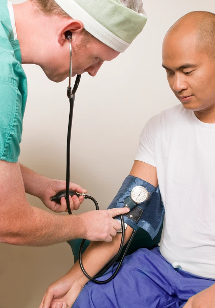 A white male nurse wearing a green shirt takes the blood pressure of an Asian man