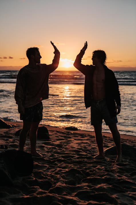 Silhouette of two men on the beach are about to high five during sunset