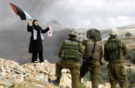 A Palestinian woman stands in front of armed and violent Israeli soldiers during protest holding a Palestinian flag in the West Bank village of Bilin, against Israel's Gaza massacre of January 2009.
