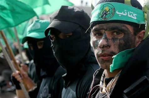 Young male Palestinian soldiers wear green head bands and cover their faces with black cloth or dirt. They hold large green flags.