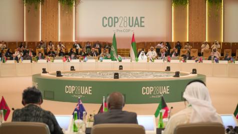 Nations leaders sit at a plenary for the Global Stocktake at COP 28 in Dubai. There is a large round green table in the centre and the leaders all sit on the outskirts with their respective flags infront of them