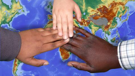 Three hands of different skin colour touch in the centre of a map of the world