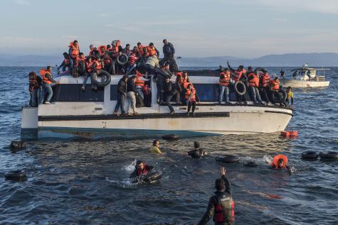 Syrian and Iraqi refugees arrive from Turkey to Lesbos island, Greece by boat. Volunteers are in the water helping them to reach the shore.