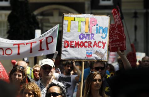 TTIP protest in London. Many protesters gather in the street holding signs. One says 'TTIPing over democracy'