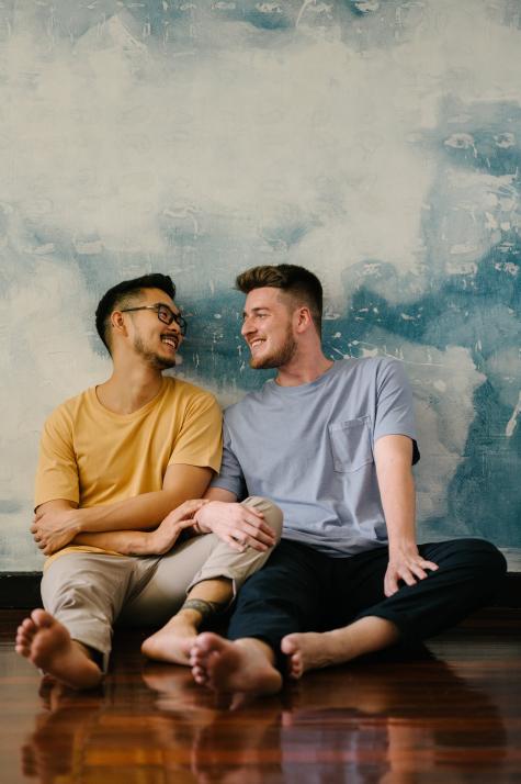 Two men sit on the floor smiling