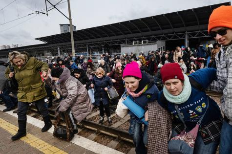 Ukrainian families, mostly women, desperately run across train tracks at a station to get to the next westbound train in Kyiv