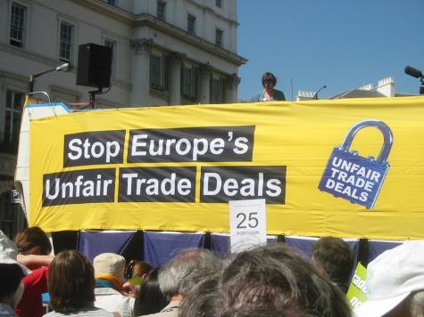 Protesters stand infront of a large yellow banner which reads 'Stop Europe's Unfair Trade Deals'
