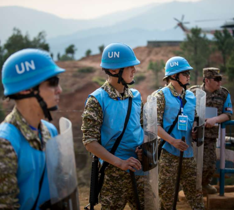 Four United Nations peacekeepers stand in a field wearing protective gear and the signature blue helmets