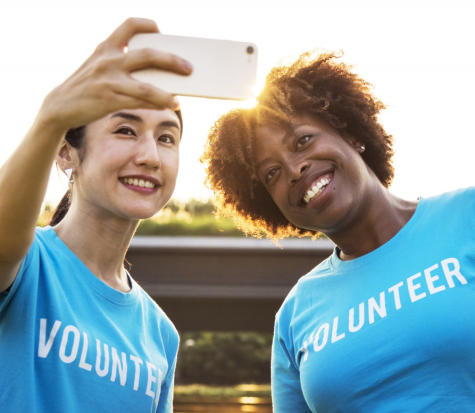 An Asian and a black woman take selfie wearing blue tshirts which say 'volunteer' in white. They are both smilling into the camera.