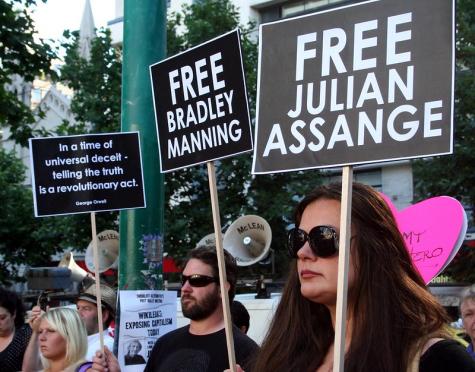 Many supports of Julian Assange and Bradley Manning rally at the British consulate. A man and a woman in the foreground of the other protestrs hold signs saying 'Free Julian Assange' and 'Free Bradley Manning'.