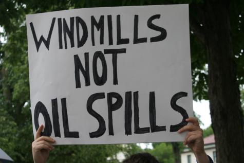 A protester holds a large white sign which reads 'Windmills not oil spills'