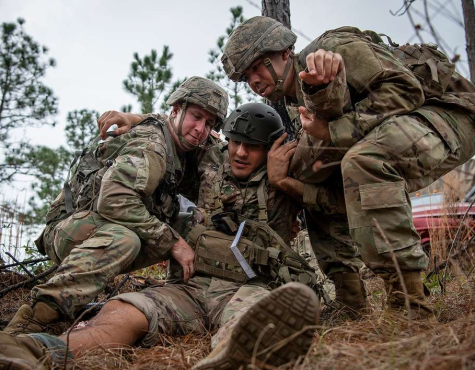 Two soldiers help a simulated wounded victim up during a mass casualty exercise