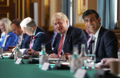 A cabinet meeting London where Boris Johnson and Rishi Sunak sit next to each other at a long green table. They are sitting infront of microphones, smiling, and are both wearing suits