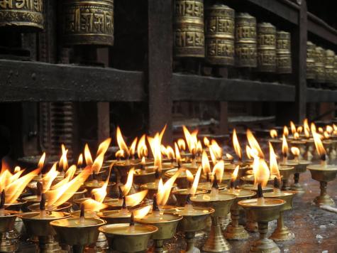 Many tea light candles are lit infront of traditional prayer wheels in Nepal
