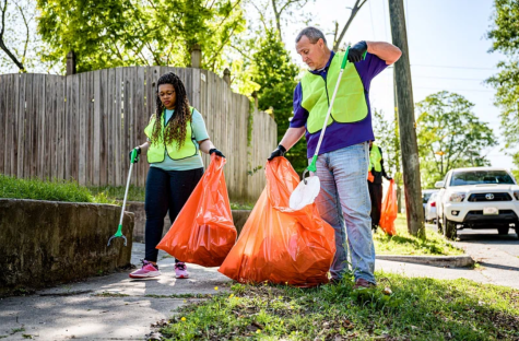 A man and a woman wearing yellow high-vis jackets carry bin bags and collect rubbish from their local community