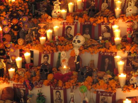 An altar in Oaxaca, Mexico has been made to honour and celebrate the lives of the dead. There are several photographs in frames surrounded by orange flowers, candles, and decorative skulls