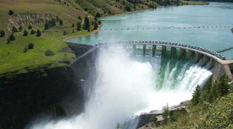 A huge hydroelectric dam lets huge amounts of water pass whilst holding back the lake of the reservoir surrounded by green fields