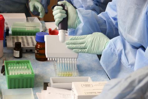 Close up image of two people wearing protective gear and latex gloves using trsting equipment in a laboratory
