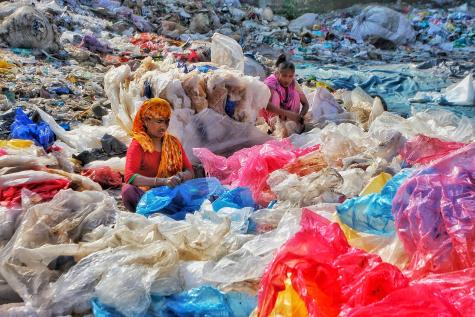 Two Asian women wearing colourful clothing sit in a landfill site sorting through plastic waste