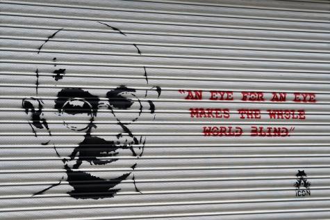 Artwork of Gandhi spraypainted on a metal shutter. The quote 'An eye for an eye makes the whole world blind' is sprayed in red.