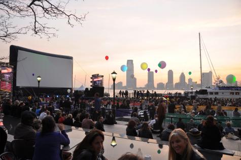 A large outdoor screen sits by the waterside at the Tribeca Film Festival where on lookers sit and wait for the film to start