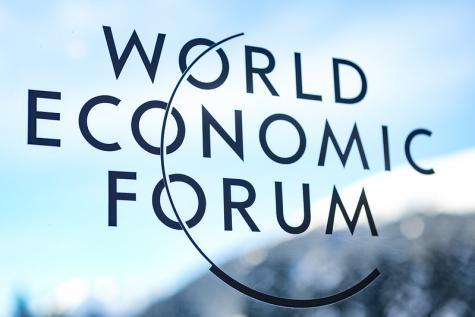 The World Economic Forum logo taken from a window with a snowy mountain in the background. The words are written in black and there is semi circle going through them 