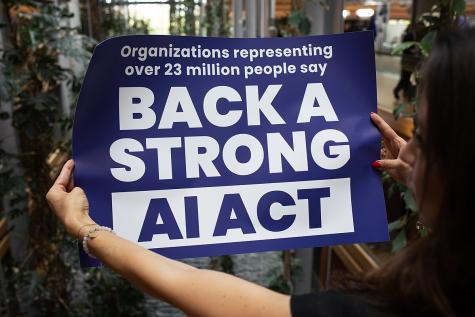 A woman holds up a large blue sign that says 'Back a strong AI Act'.