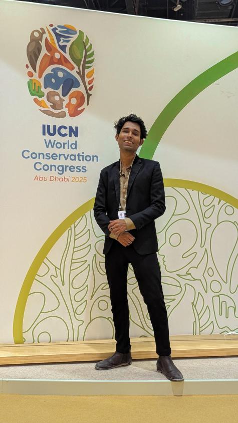 The author posing in front of the main banner of the IUCN World Conservation Congress 2025 in Abu Dhabi