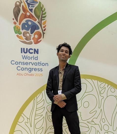 Author Tanuj Samaddar posing in front of the main banner of the World Conservation Congress 2025 in Abu Dhabi