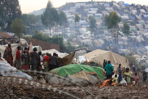 A refugee camp full of Congolese refugees. There are many tents in an area which is surrounded by barbed wire. The camp sprawls across the mountains.