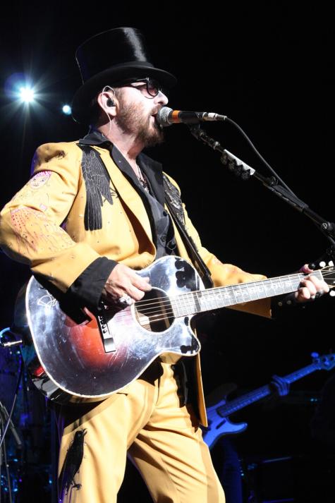 Musician Dave Stewart performs on stage wearing a yellow suit and a black top hat.