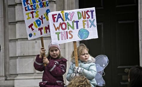 Two little girls stand holding signs at a climate protest. The sign at the front says 'Fairy Dust wont Fix This'