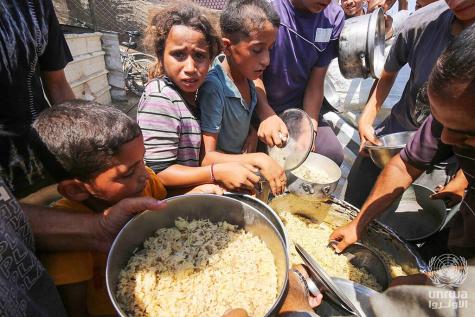 Displaced Palestinians in Deir el-Balah line up to receive food provided by charitable organizations
