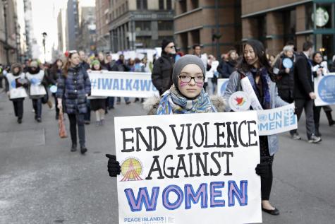 Protesters line the streets of New York for International Women's Day. A woman at the front is holding a large sign that says 'End violence against women'.