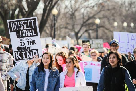 Protesters line the streets at a women's rights demonstration. There are many posters but in the foreground there is a large white one that says 'Intersectional feminism is the only kind'. 