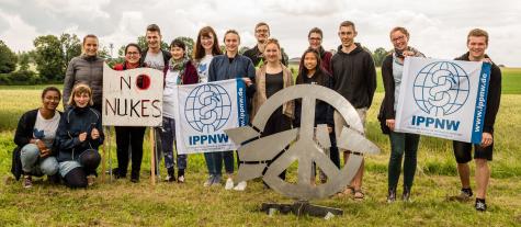 IPPNW protest in Büchel 2018. Anti-nuclear activists stand in a field holding signs advocating for no more nukes.