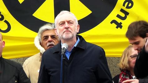Jeremy Corbyn speaking at the #StopTrident rally at Trafalgar Square in February 2016. He stands infront of a large yellow CND poster.